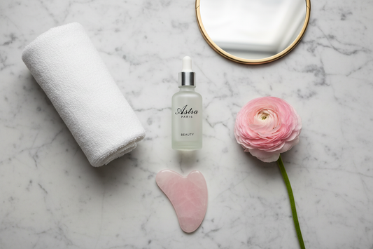 Vue de dessus (flatlay) très esthétique d’un flacon de sérum à l’acide hyaluronique “Astra Paris Beauty” posé sur une surface en marbre clair, avec à côté une serviette blanche roulée, une fleur blanche ou rose, un gua sha en quartz rose et un petit miroir. Composition minimaliste, tons blancs, beiges et rose poudré, lumière naturelle, style Instagram skincare haut de gamme, sans aucun texte ni élément graphique ajouté.